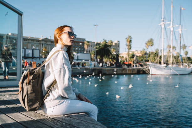 考虑女性游客在时尚的服装坐在港口码头附近，思考旅行度假的好处，有吸引力的白人女性在城市码头享受娱乐时间图片下载
