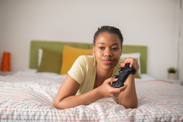 一个美丽的非裔美国妇女在家里玩电子游戏的肖像，有乐趣。图片下载