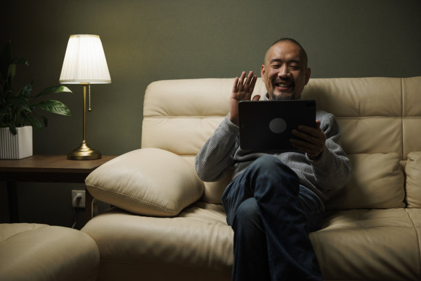 中年男子坐在沙发上用平板电脑举行视频会议图片下载