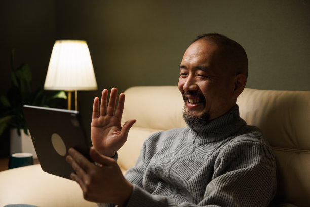亚洲中年男子坐在沙发上用平板电脑视频通话图片下载