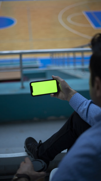 特写商人坐在篮球场上看手机，模拟屏幕图片下载