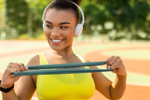 微笑的黑人妇女戴着耳机，带着橡皮筋锻炼图片下载