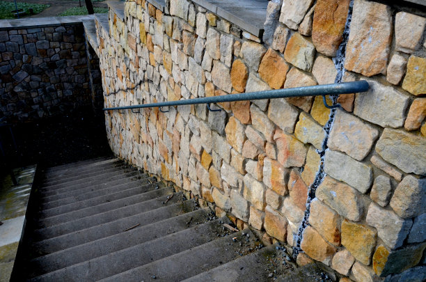 木板栅栏跟随砂岩砌成的墙，在几个地方开裂，地形的运动和高速公路车辆的振动。草坡和向下倾斜的高墙图片下载