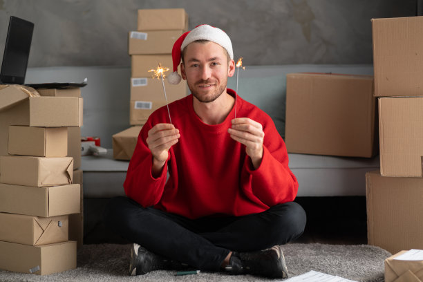 企业家小企业主圣诞老人与烟火在家里的一个小办公室。准备装运的箱子。圣诞节大减价。家庭办公室是网上商店的卖家。图片下载