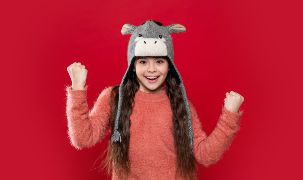 成功的青少年模特在耳盖帽。戴着耳盖帽的少年儿童被隔离在红色背景上。图片下载