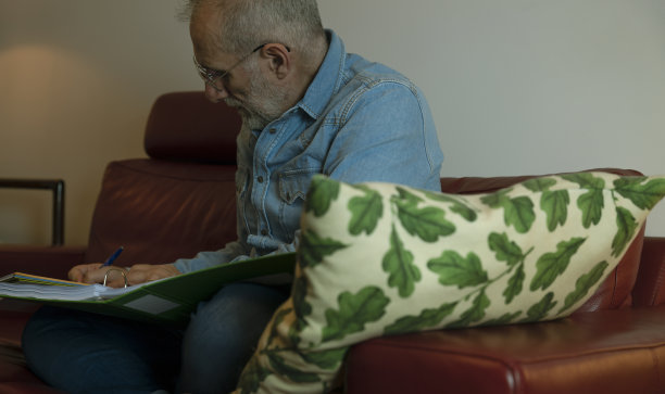 成年男子坐在家里的沙发上阅读文件文件的肖像。图片下载