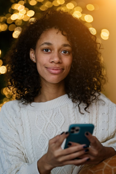 一名非裔美国妇女在舒适的客厅的圣诞树旁用智能手机聊天图片下载