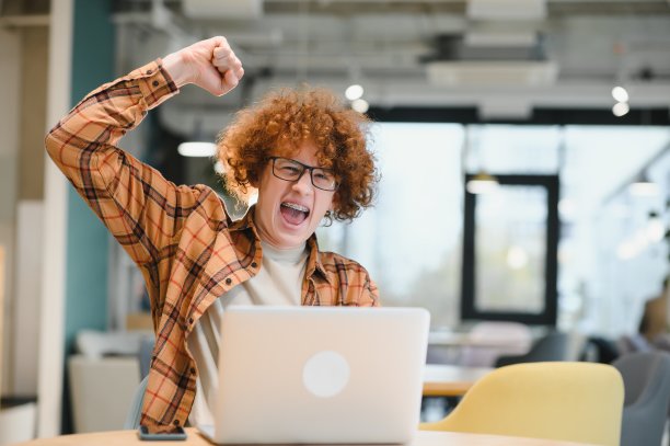 年轻快乐的男性自由职业者在便装坐在咖啡馆与笔记本电脑和使用手机。图片下载