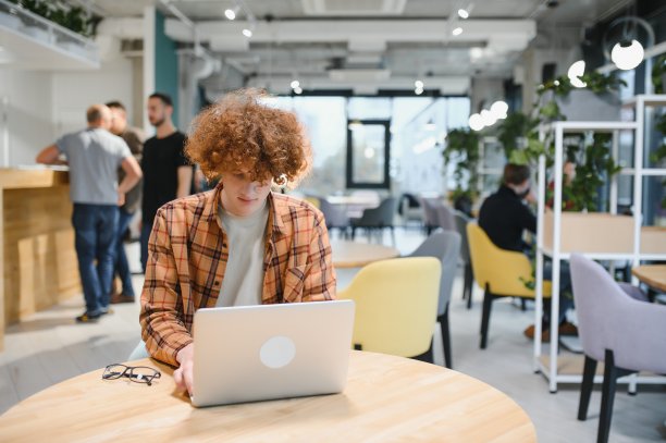 穿着时尚服装的白人男性自由职业者坐在餐厅桌子旁，为公共网站编程设计远程工作，熟练的软件开发人员在联合办公空间里摆姿势。图片下载