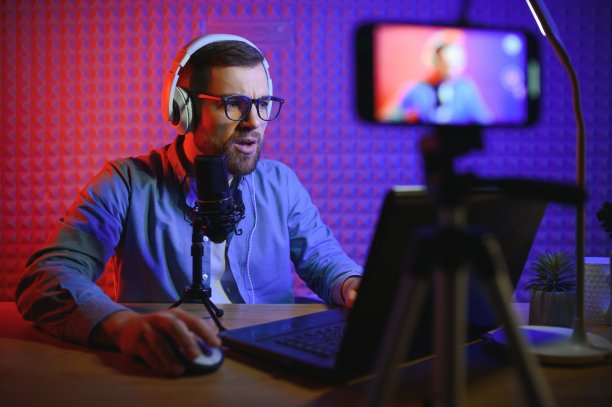 视频博主使用智能手机在工作室拍摄播客。博主用手机、麦克风和耳机拍摄社交媒体广播事业视频。图片下载