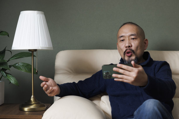 亚洲中年男子坐在沙发上用手机开视频会议图片下载