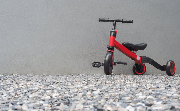 一辆红色的儿童自行车，家里后面有水泥墙。母亲教儿子骑自行车图片下载