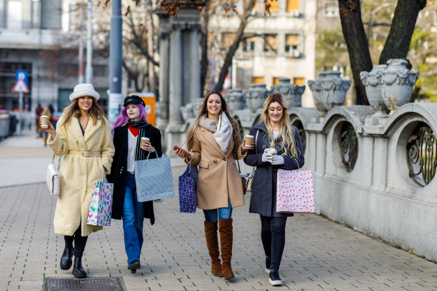 四个女性朋友愉快地走在城市的街道上，手里端着咖啡。图片下载