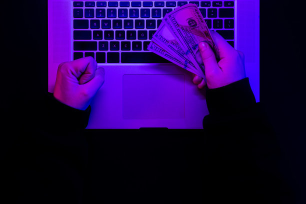 霓虹灯下的笔记本电脑键盘背景上，男性手中的钱。图片下载