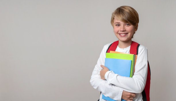 小学微笑的男孩在灰色背景的背包和练习彩色书籍。文案空间为广告空白概念。回到学校。童年，教育，产品为儿童图片下载