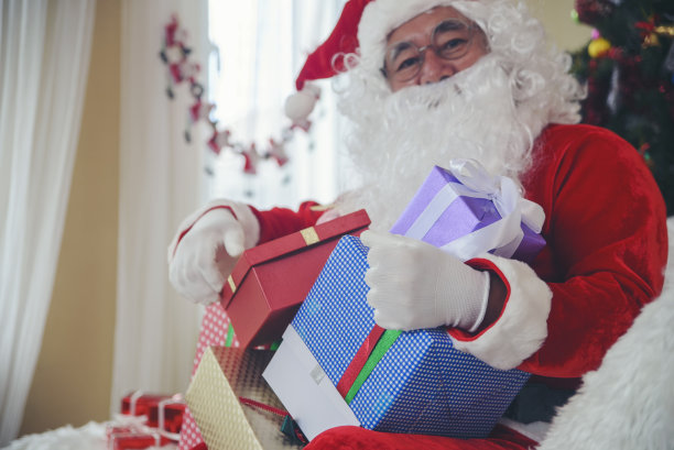 圣诞老人手拿礼盒和礼物袋给人们在圣诞节活动。图片下载