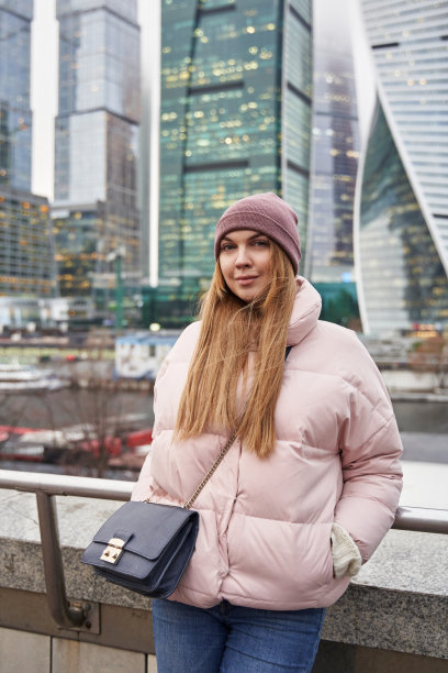 冬日里的年轻女子躲在高高的玻璃建筑和摩天大楼后面图片下载