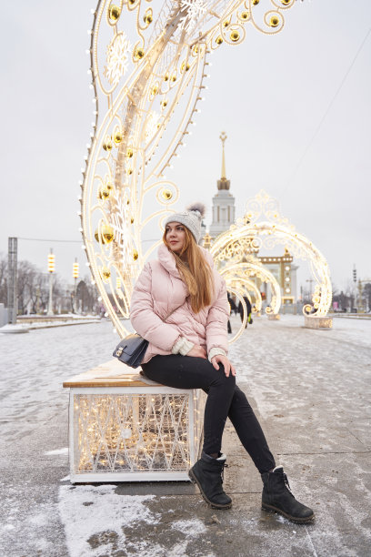 冬天里，一位美丽的年轻女子坐在城市里的圣诞装饰灯的背景下。节日照明。美丽的发光雪花图片下载