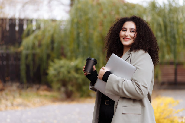 一位女商人端着一杯咖啡，手里拿着一台笔记本电脑图片下载