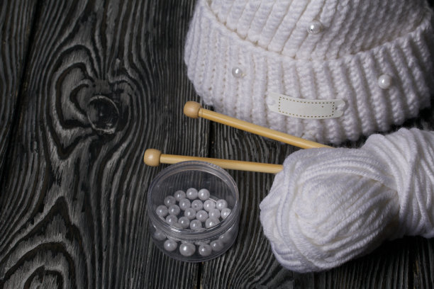 白色针织围巾。女式手工针织服装。旁边有一捆用来编织的白线和针织针。在黑板上。图片下载