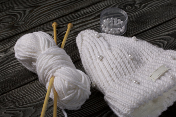 白色针织围巾。女式手工针织服装。旁边有一捆用来编织的白线和针织针。在黑板上。图片下载