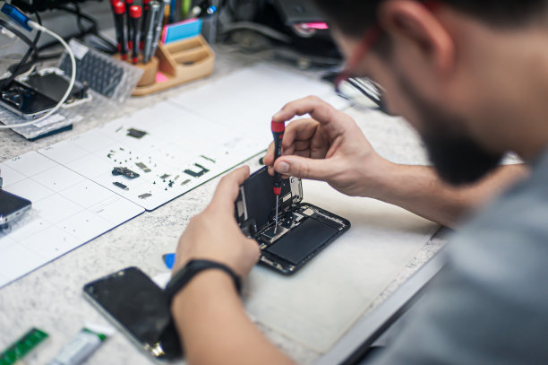 在电子修理厂，修理工用螺丝刀拆卸智能手机图片下载