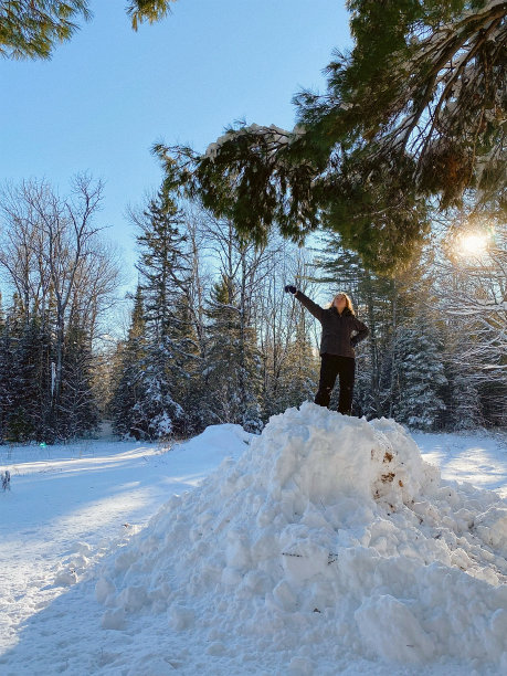 一个十几岁的女孩站在一个巨大的雪堆上，手臂举起来。图片下载