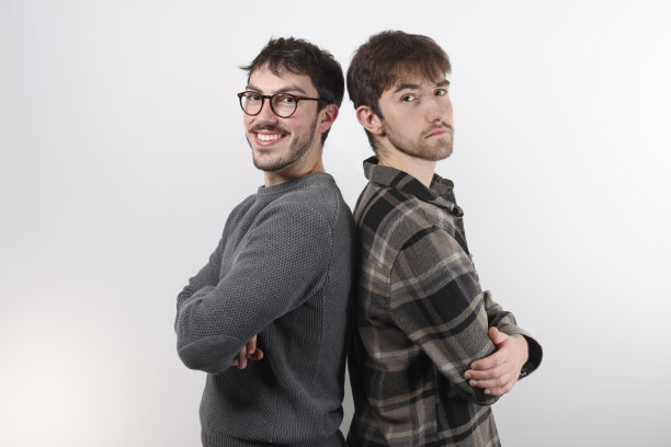 两个年轻的朋友背靠背，微笑着，双臂交叉。孤立的，白色背景图片下载