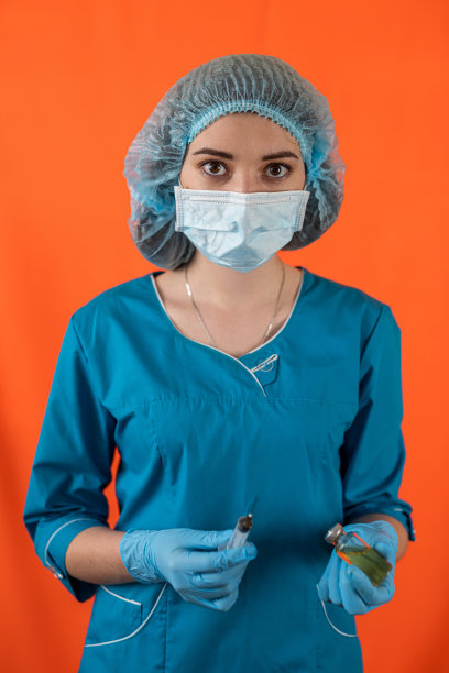 带着注射器的女医生在彩色演播室背景上为相机摆姿势。图片下载