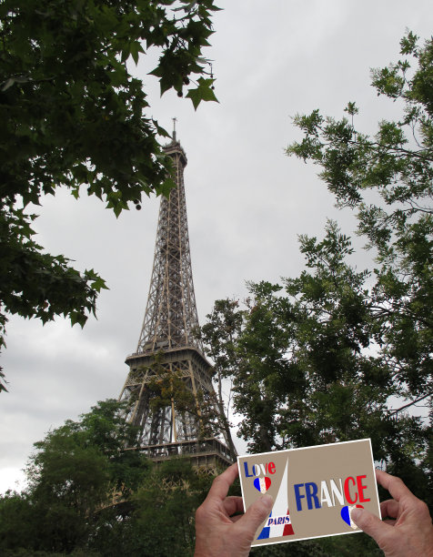 埃菲尔铁塔前，人们手拿一张写有“爱法国巴黎”的明信片图片下载