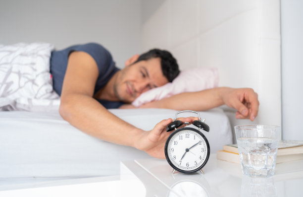 Young Man Reaching For Her Alarm Clock After Waking Up İn Bed At Home图片下载