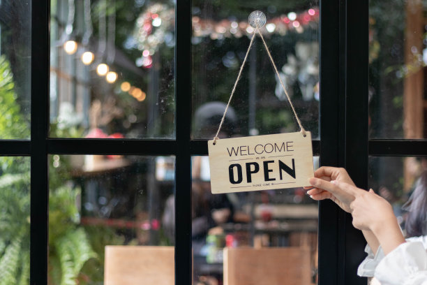 咖啡店职员们正在翻动安装在玻璃前门上的开店标志，以便顾客可以看到开店标志，并在咖啡店内使用服务。创业理念。图片下载