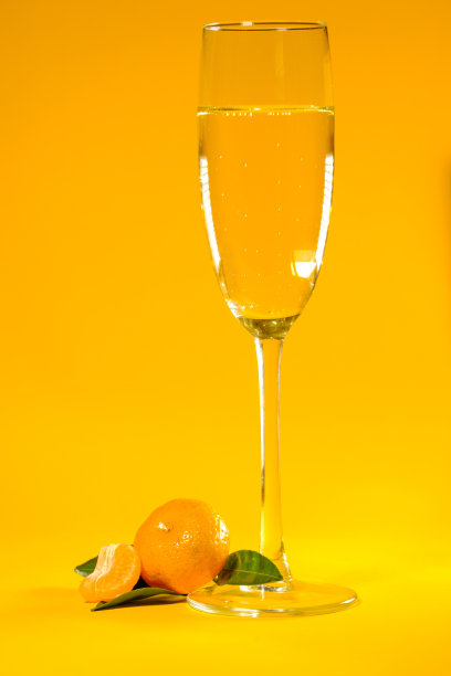 成熟的小柑橘，绿叶，一杯香槟，黄色背景图片下载