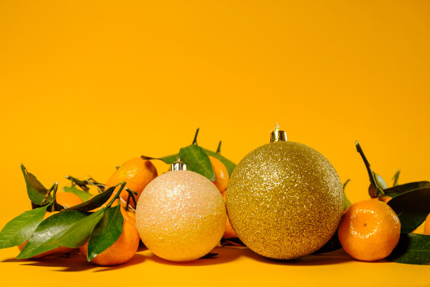 成熟的小橘子，绿色的叶子和黄色背景上的圣诞球图片下载