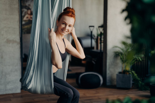 快乐的红头发女人坐在空中瑜伽吊床图片下载