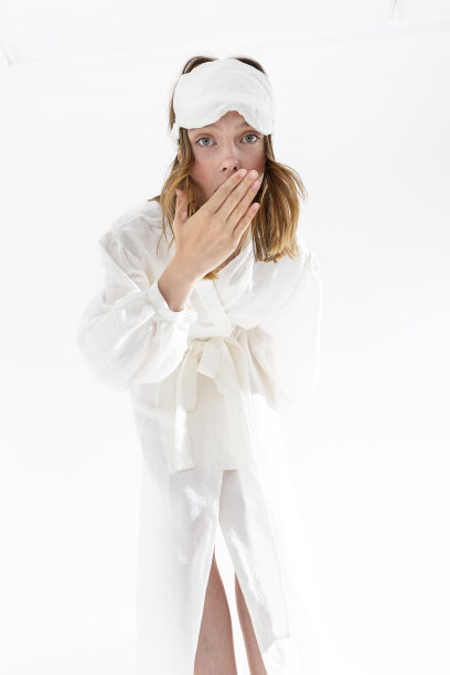 漂亮的年轻女子在丝绸织物白色睡衣和睡眠面具看着相机。图片下载