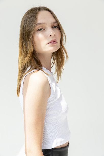 白色背景下，一个满脸雀斑的金发女孩穿着白色短袖上衣和黑色皮裤。图片下载