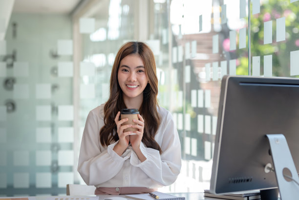 年轻的亚洲女商人在办公室工作时喝咖啡休息。看着镜头。图片下载