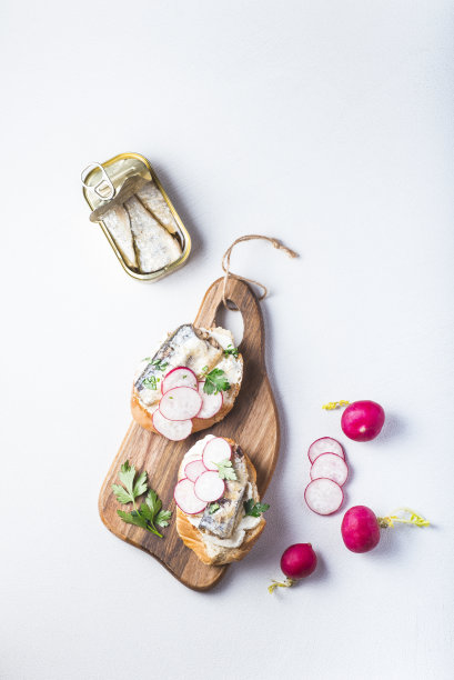 Canned sardines and simple canned fish recipes. Mini sandwiches with sardines, radishes and curd cheese.  Easy and healthy lunch. Сanned or tinned fish  is one of the food trends of 2023, top view, white table图片下载