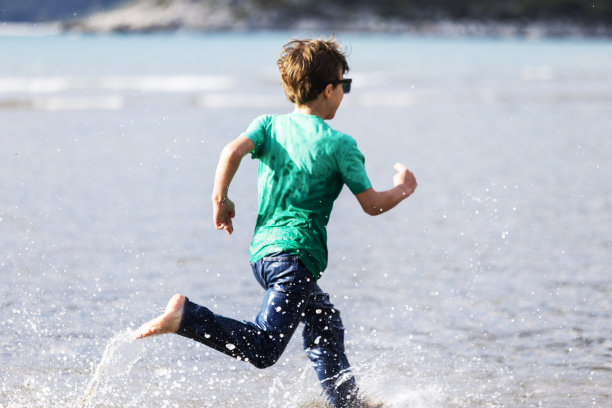 十几岁的男孩在沙滩上的水里奔跑图片下载