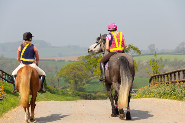 两名年轻女子喜欢一起骑马在英国乡村骑行，她们穿着色彩鲜艳的荧光装备，以确保被人看到和安全。图片下载