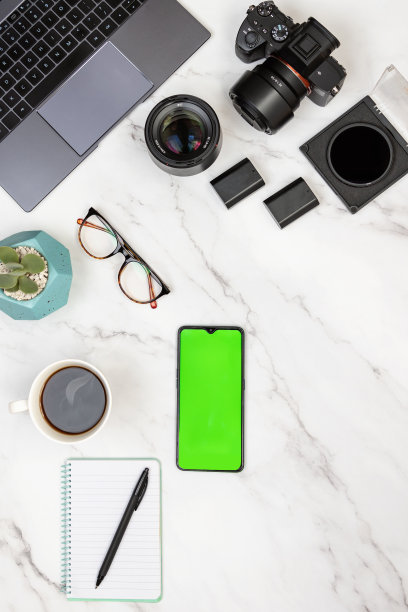 现代白色大理石摄影师工作区，笔记本电脑，相机，记事本，热咖啡和带有绿色屏幕的彩色键的手机。图片下载