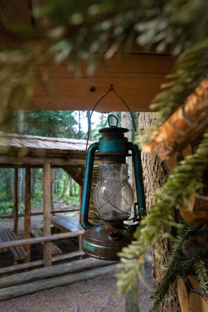 老煤油灯挂在木屋的角落里，木屋旁边是树林里的凉亭。垂直图图片下载