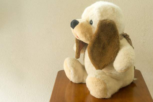 可爱的小狗娃娃坐在椅子上，一边对着房间的墙壁，复制文本的空间。可爱的毛绒小狗娃娃，供孩子或小朋友玩耍图片下载