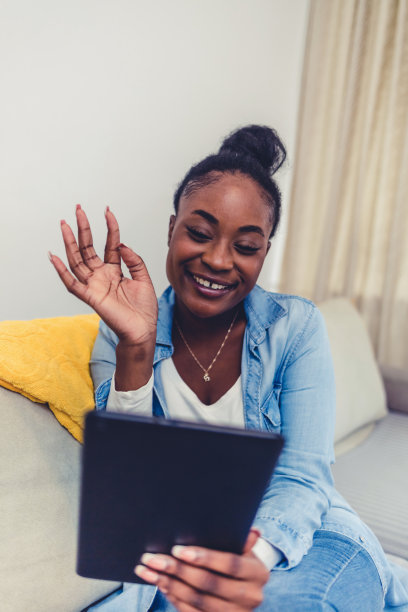 在家工作。一位年轻女子用平板电脑阅读/观看内容。微笑的非裔美国妇女忙着浏览平板电脑。图片下载