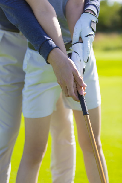 近距离的高尔夫俱乐部和手，高尔夫教练和高尔夫球手，一对夫妇在阳光明媚的白天高尔夫球场的绿色练习高尔夫-股票照片图片下载