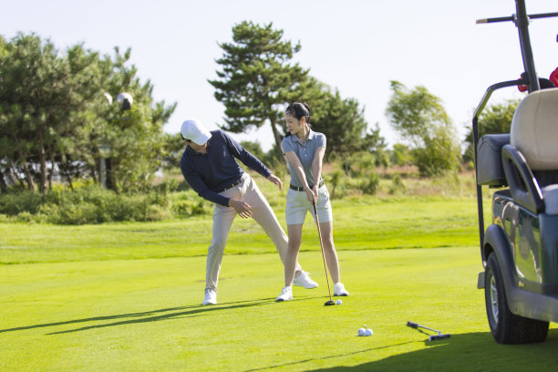 一个年轻的东亚男人和女人练习高尔夫在阳光明媚的白天高尔夫球场，教练和学生的股票照片图片下载