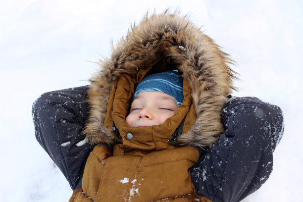 一个英俊的男孩躺在雪地上，双臂交叉放在脑后。他闭上眼睛笑了。图片下载