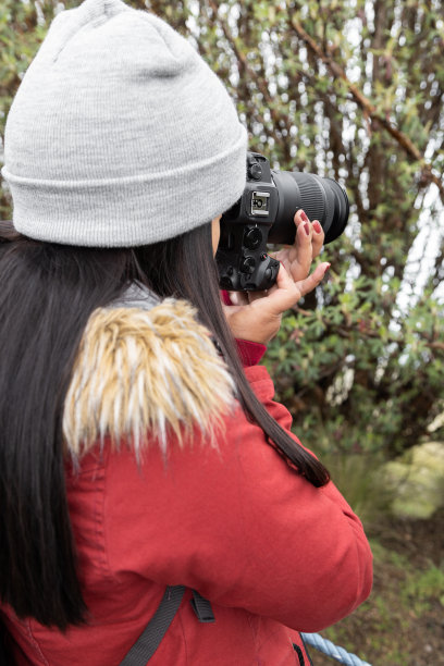 在农村工作的年轻女子头戴羊毛帽，留着长发，手持专业相机图片下载