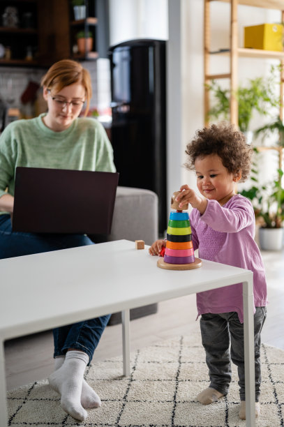 妈妈在笔记本电脑上工作，而她可爱的小女儿正在玩一个教育说教玩具图片下载